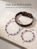 The Sacred Light crystal bracelet with amethyst
grey moonstone beads and silver cross charm,
divine protection intuition bracelet
on soft purple fabric surface