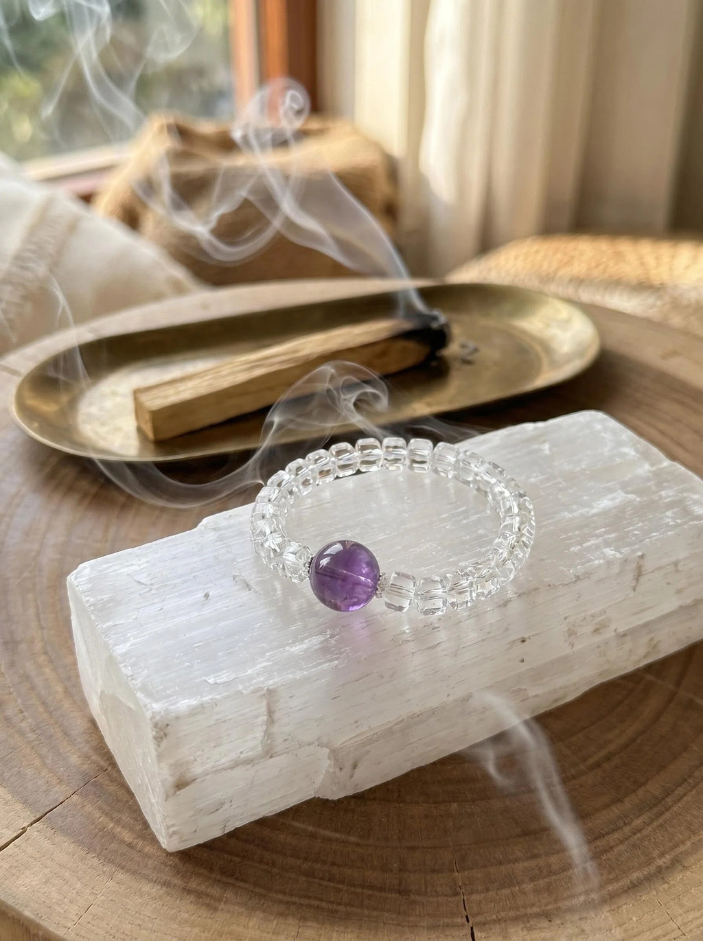 Still Mind amethyst and clear quartz bracelet
on selenite charging plate with white sage bundle,
crystal bracelet cleansing ritual purple and white tones