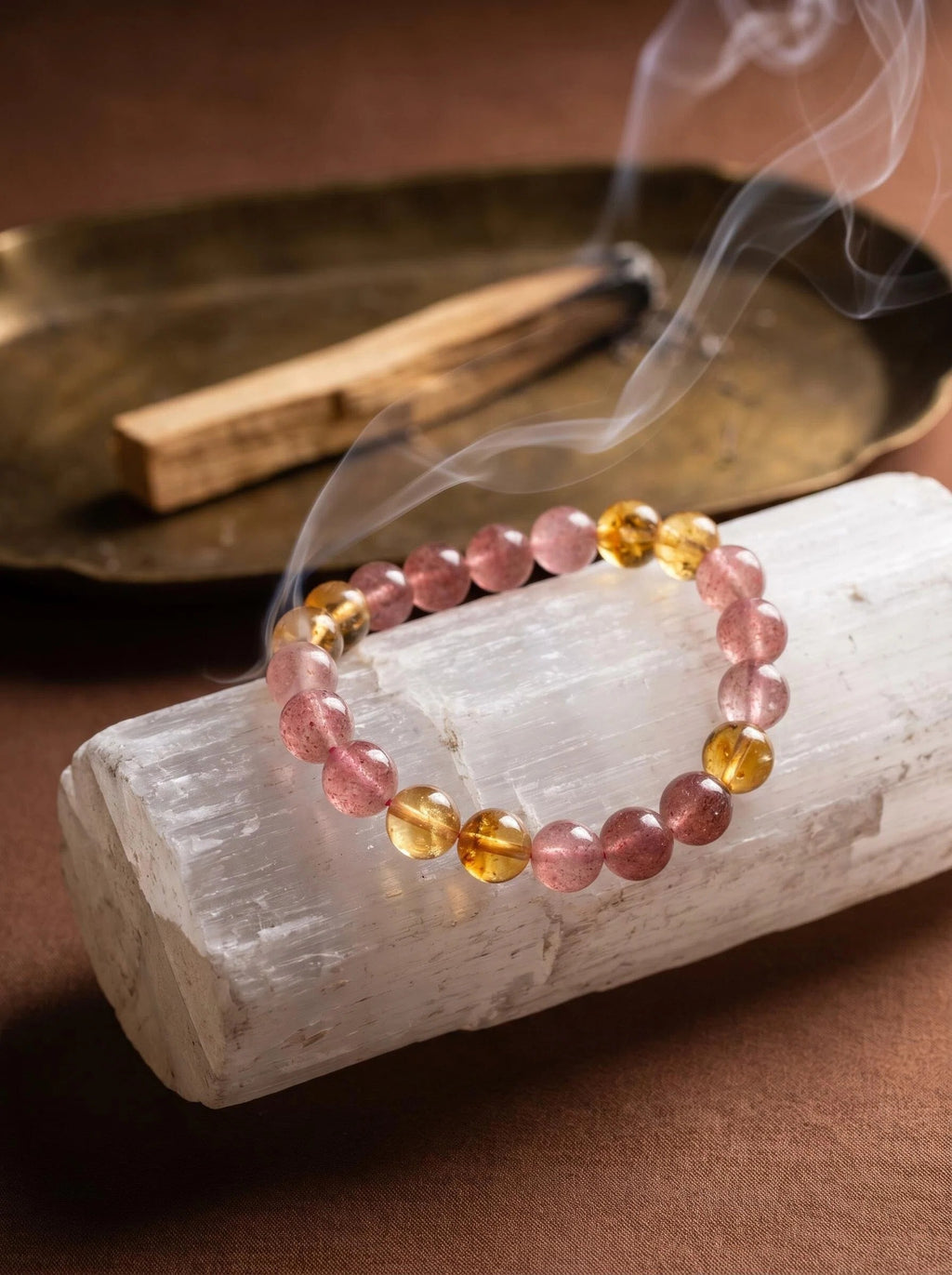 Warm Light crystal bracelet on selenite charging plate
with palo santo smoke and amber piece,
crystal bracelet cleansing ritual warm golden tones