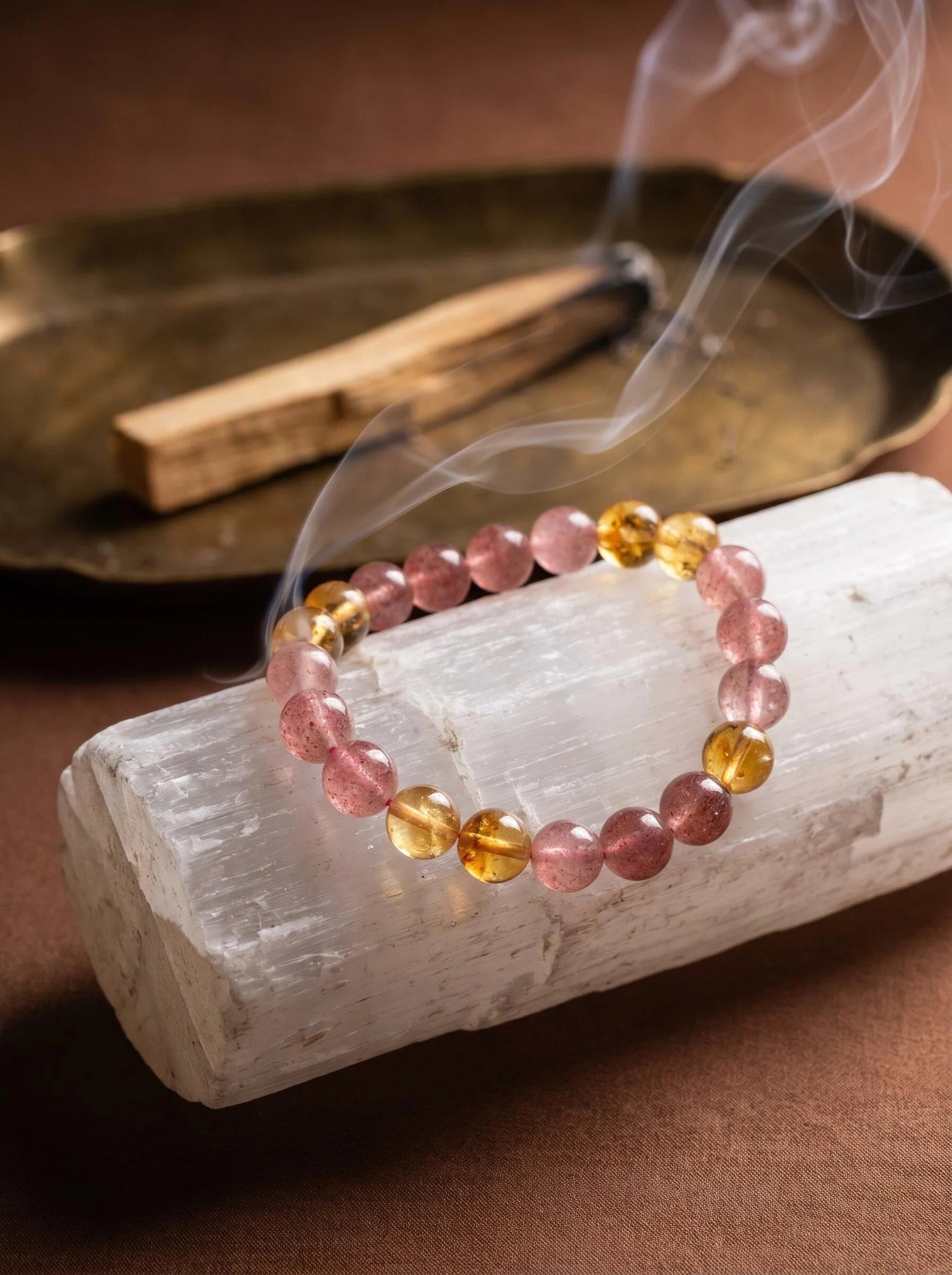 Warm Light crystal bracelet on selenite charging plate
with palo santo smoke and amber piece,
crystal bracelet cleansing ritual warm golden tones